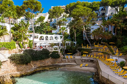 Kleine Bucht mit Steinfelsen auf deinen gelbe Sonnenschirme und Liegen stehen und altes Geb&auml;ude zu sehen ist